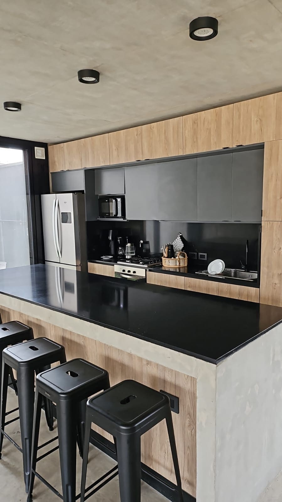 Cocina de madera natural con isla de material de granito con sillas